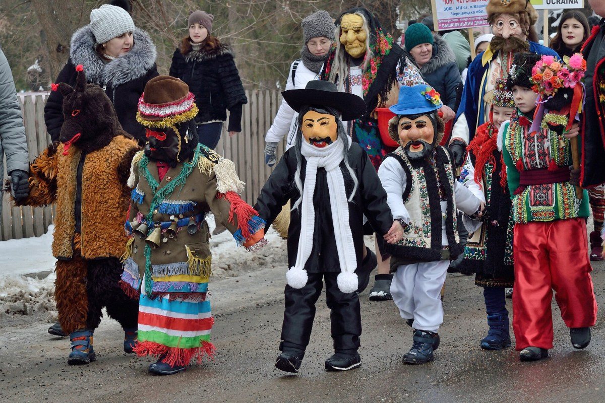 Costumed participants of the Malanka folk carnival walking through a snowy street in Bukovina.